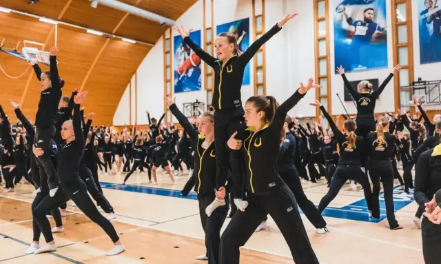 Voimistelijoita yhtenäisissä mustissa asuissa harjoittelemassa liikesarjaa Kisakallion urheiluhallissa